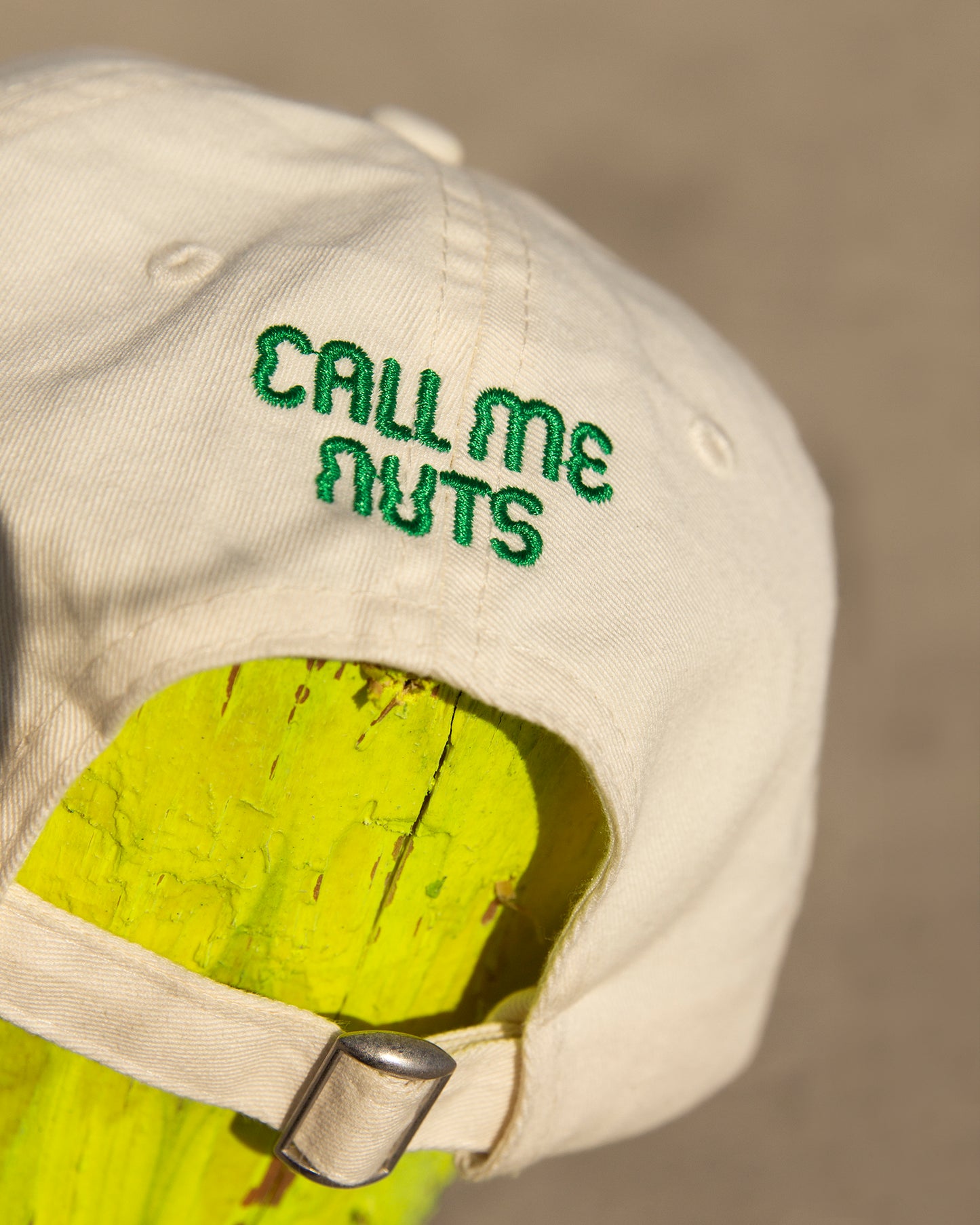 Beigefarbene Cap mit grünem CALL ME NUTS Stick hinten.