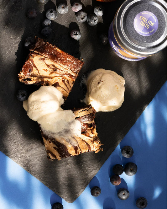 Peanut Butter Brownie mit Vanilleeis und Heidelbeeren auf blauem Untergrund.