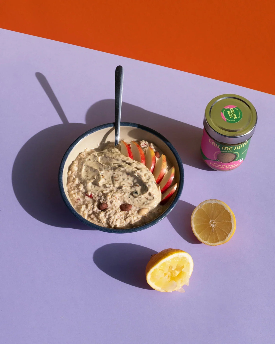 FULL POWER Bircher Müsli in einer Schüssel, ein Glas Peanut Butter und eine aufgeschnittene Zitrone.