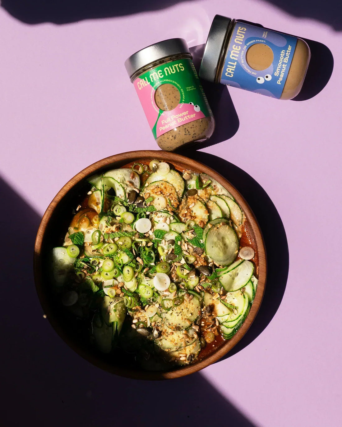 Gurkensalat in einer großen Schüssel und zwei Gläser Peanut Butter, die neben der Schüssel liegen.