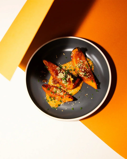 Geröstete Kürbisspalten mit Erdnussauce auf einem grauen Teller