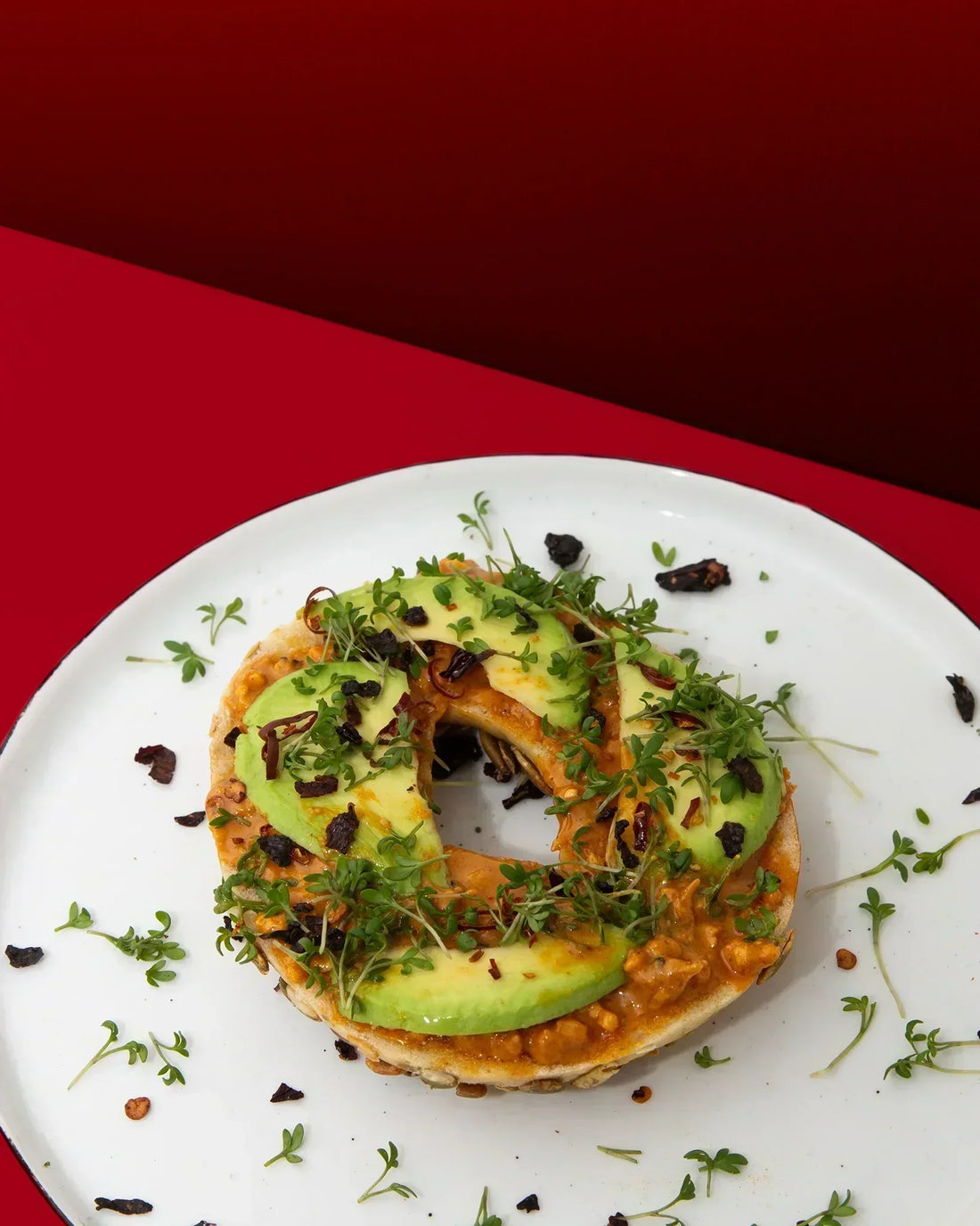 Bagel mit Smokin' Hot Peanut Butter, Avocado und Kresse auf einem weißen Teller.
