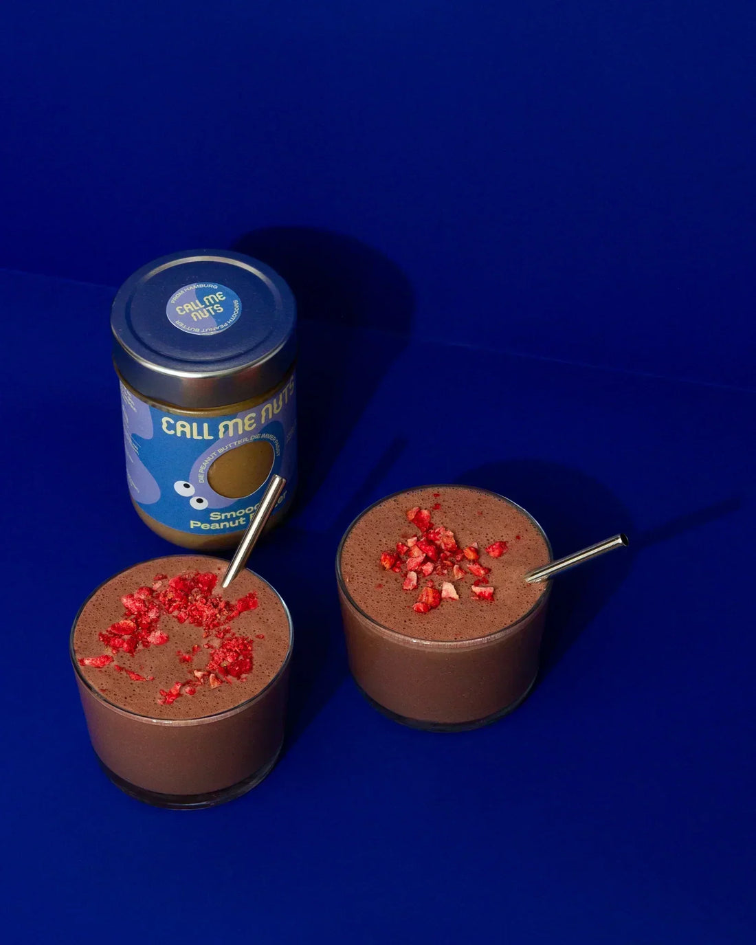 Zwei Gläser mit Chocolate Peanut Butter Smoothie vor blauem Hintergrund.