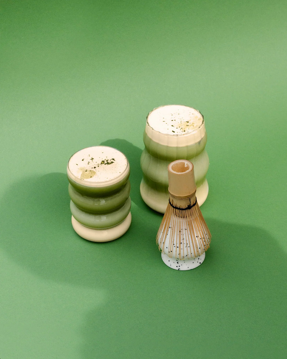 Zwei Gläser mit Peanut Butter Matcha Latte vor einem grünen Hintergrund