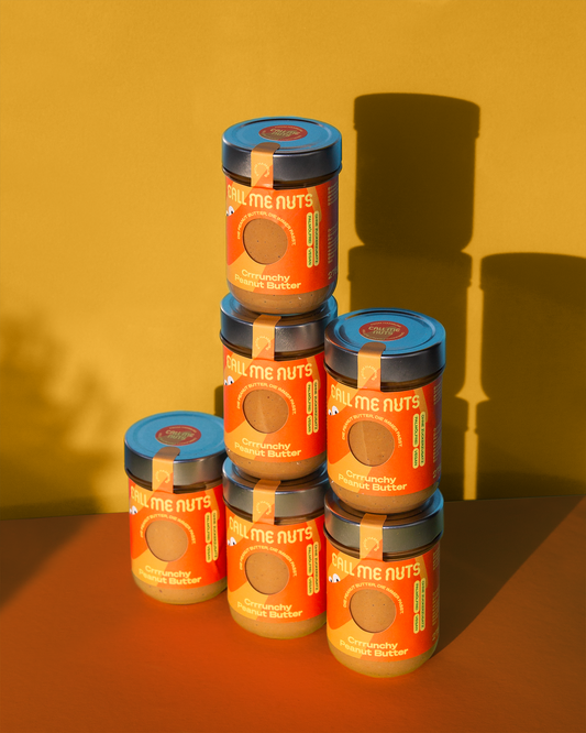 Sechs Gläser Crrrunchy Peanut Butter vor orange-gelbem Hintergund