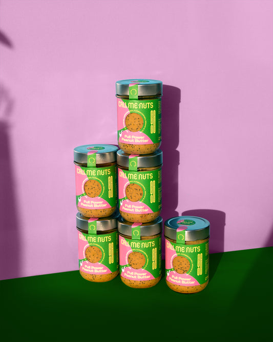 Sechs Gläser Full Power Peanut Butter vor rosa-grünem Hintergund
