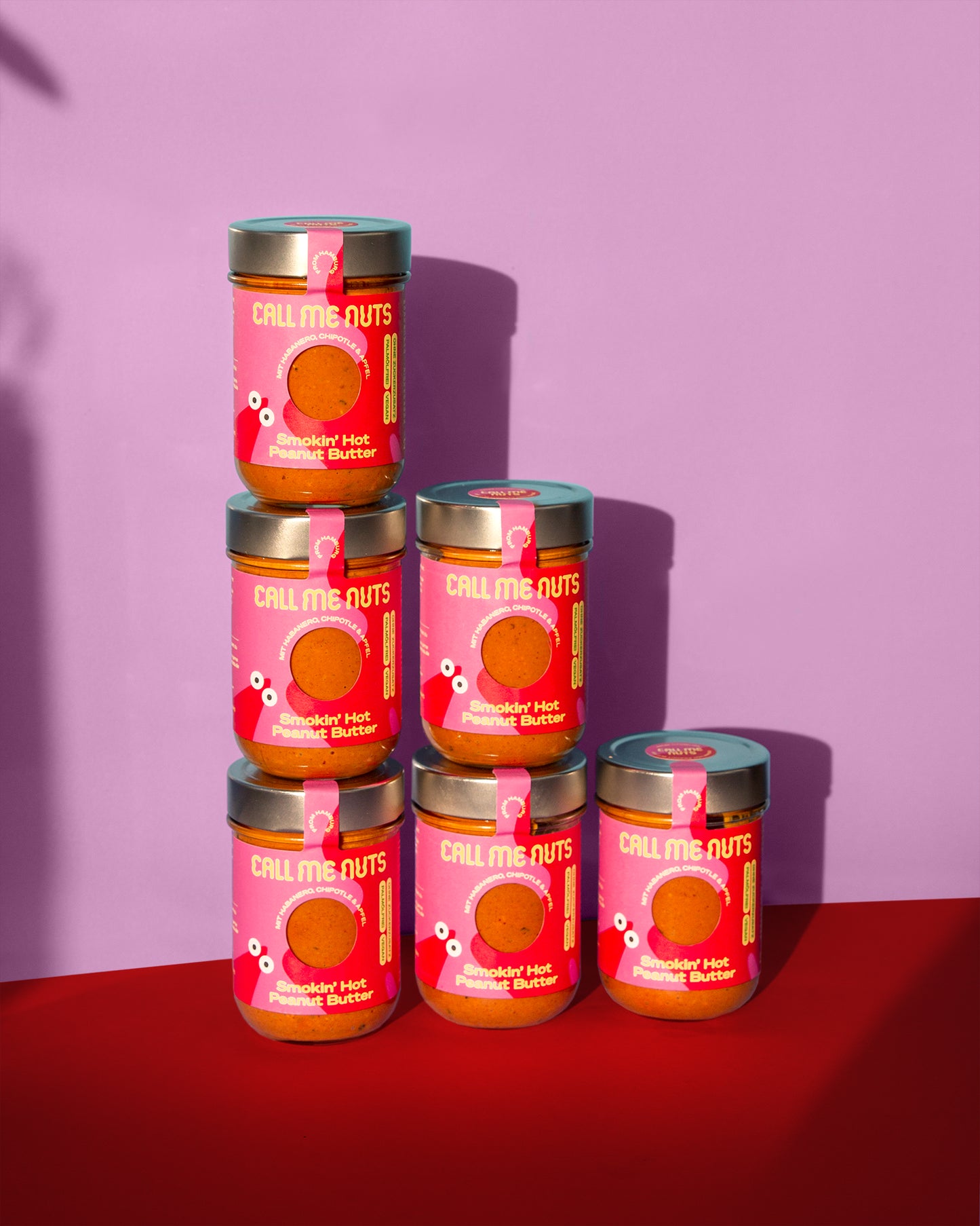 Sechs Gläser Smokin' Hot Peanut Butter vor rosa-rotem Hintergund