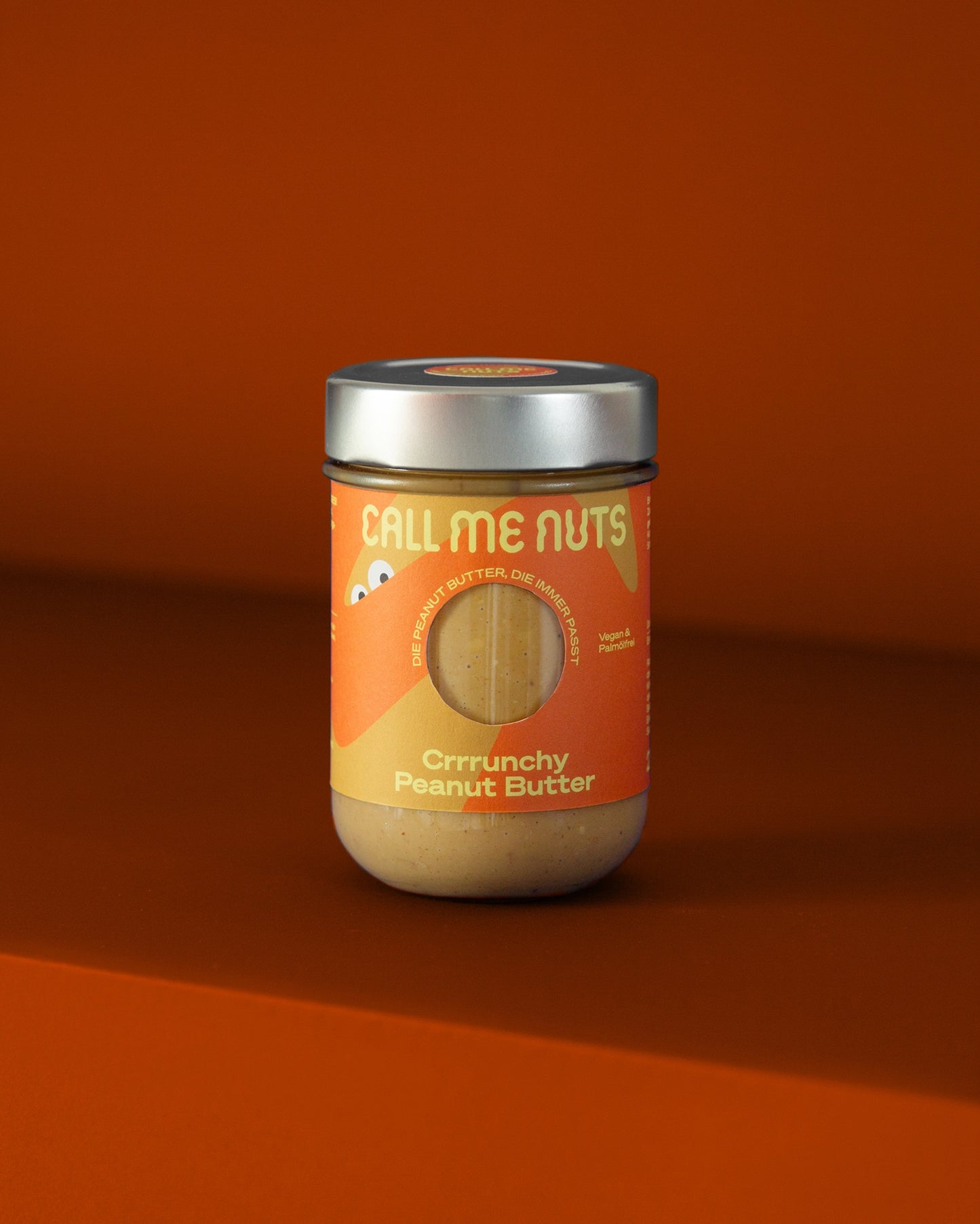 Peanut Butter Glas Crrrunchy vor orangefarbenem Hintergrund.